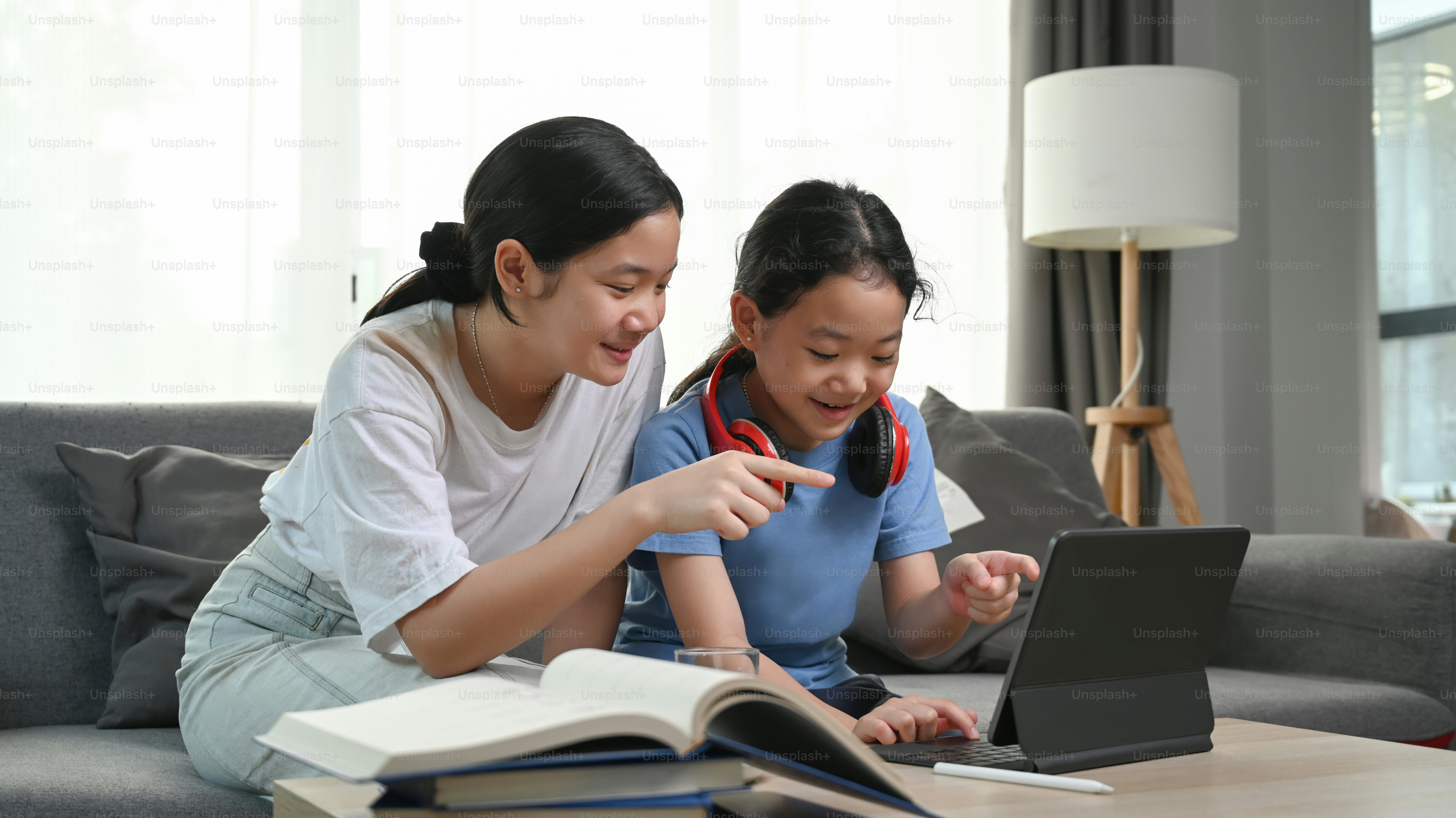 Two young girls sitting on sofa and watching something funny on digital tablet together.